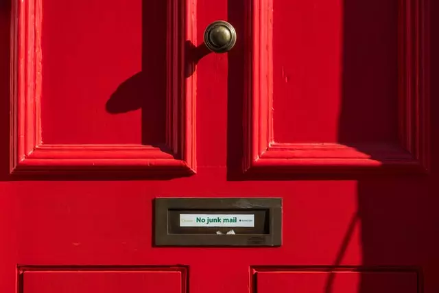 Auf dem Briefschlitz einer roten Tür klebt ein Aufkleber mit "No Junk Mail"