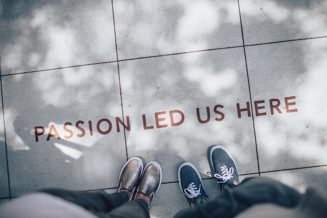 Zwei Personen stehen auf grauen Betonplatten, auf denen der Schriftzug "Passion led us here" steht